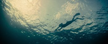 Movie still from “No Limit” (2022), directed by David M. Rosenthal – A person swimming in the ocean under the water; Extreme Wide shot, Overhead angle