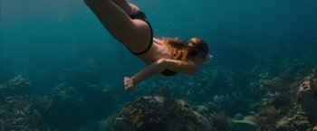 Movie still from “No Limit” (2022), directed by David M. Rosenthal – A woman in a black bikini swimming in the ocean; Medium shot, Overhead angle
