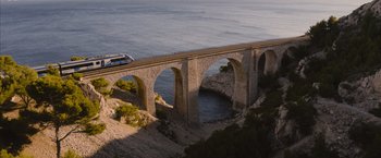 Movie still from “No Limit” (2022), directed by David M. Rosenthal – A train traveling over a bridge over a body of water; Extreme Wide shot, High angle