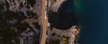Movie still from “No Limit” (2022), directed by David M. Rosenthal – An aerial view of a train crossing a bridge; Extreme Wide shot, Overhead angle