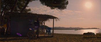 Movie still from “No Limit” (2022), directed by David M. Rosenthal – A man standing on a beach next to an umbrella; Extreme Wide shot, Low angle
