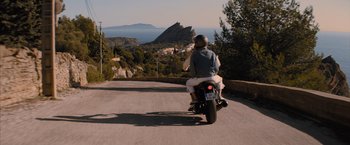 Movie still from “No Limit” (2022), directed by David M. Rosenthal – A person riding a motorcycle down a street; Wide shot, High angle