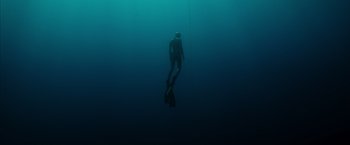 Movie still from “No Limit” (2022), directed by David M. Rosenthal – A man in a wetsuit swimming in a body of water; Wide shot, Low angle