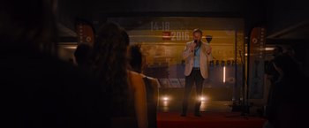 Movie still from “No Limit” (2022), directed by David M. Rosenthal – A man standing on a stage holding a wine glass; Wide shot, Over the shoulder angle