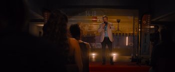 Movie still from “No Limit” (2022), directed by David M. Rosenthal – A man standing on a stage holding a microphone; Wide shot, Over the shoulder angle