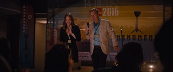 Movie still from “No Limit” (2022), directed by David M. Rosenthal – A man and a woman holding microphones on a stage; Medium shot, Over the shoulder angle