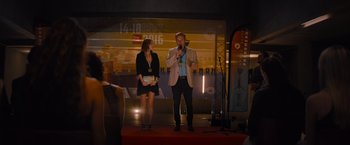 Movie still from “No Limit” (2022), directed by David M. Rosenthal – A man and a woman standing in front of a microphone on a stage; Wide shot, Over the shoulder angle