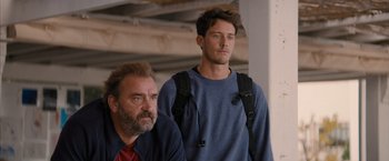 Movie still from “No Limit” (2022), directed by David M. Rosenthal – A man standing next to another man in a room; Medium shot, Low angle