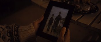 Movie still from “No Limit” (2022), directed by David M. Rosenthal – A person holding a photo of a man and a woman in wetsuits in front of the ocean; Close Up shot, High angle