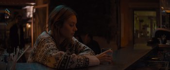 Movie still from “No Limit” (2022), directed by David M. Rosenthal – A woman sitting at a table looking at her cell phone; Medium shot, Over the shoulder angle