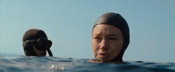 Movie still from “No Limit” (2022), directed by David M. Rosenthal – A woman in a wetsuit swimming in a body of water; Close Up shot, Over the shoulder angle