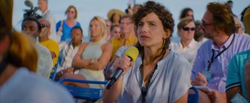 Movie still from “No Limit” (2022), directed by David M. Rosenthal – A woman holding a microphone in front of a group of people; Close Up shot, Over the shoulder angle