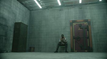 Movie still from “Atlanta” (2016), created by Donald Glover – A man sitting on a chair in a room; Wide shot, High angle