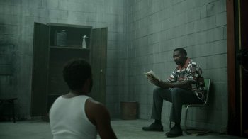 Movie still from “Atlanta” (2016), created by Donald Glover – A man sitting on a chair reading a book to a young boy; Wide shot, Over the shoulder angle
