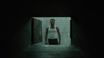 Movie still from “Atlanta” (2016), created by Donald Glover – A man standing in an open doorway in a dark room; Medium shot, Low angle