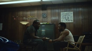 Movie still from “Atlanta” (2016), created by Donald Glover – Two men are sitting in a room and one of them is holding a card; Medium shot, Over the shoulder angle