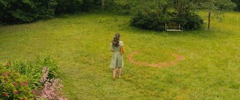 Movie still from “No One Will Save You” (2023), directed by Brian Duffield – A woman standing in the grass holding a frisbee; Extreme Wide shot, Overhead angle