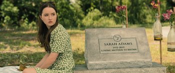Movie still from “No One Will Save You” (2023), directed by Brian Duffield – A woman sitting next to a grave stone; Medium shot, Over the shoulder angle