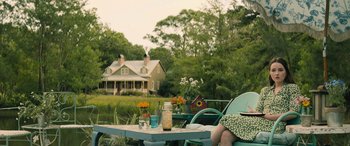 Movie still from “No One Will Save You” (2023), directed by Brian Duffield – A woman sitting at a table outside in a yard; Medium shot, Low angle