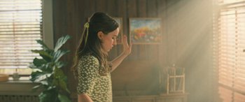 Movie still from “No One Will Save You” (2023), directed by Brian Duffield – A young girl in a green polka dot dress holding her hand up to her face; Medium shot, Over the shoulder angle