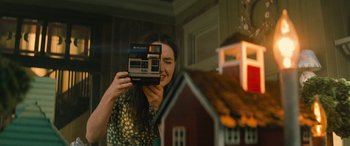 Movie still from “No One Will Save You” (2023), directed by Brian Duffield – A woman taking a picture of a model house; Extreme Close Up shot, Over the shoulder angle