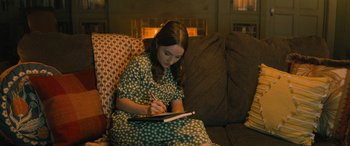 Movie still from “No One Will Save You” (2023), directed by Brian Duffield – A woman sitting on a couch writing on a notebook; Medium shot, High angle