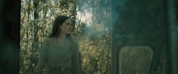 Movie still from “No One Will Save You” (2023), directed by Brian Duffield – A woman standing next to a window with trees in the background; Medium shot, Over the shoulder angle