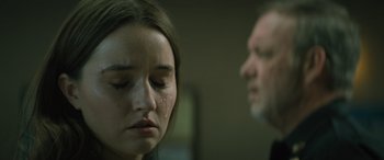 Movie still from “No One Will Save You” (2023), directed by Brian Duffield – A young woman with tears in her eyes and an older man in the background; Close Up shot, Over the shoulder angle