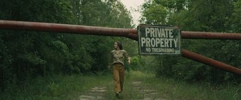 Movie still from “No One Will Save You” (2023), directed by Brian Duffield – A woman walking in the grass near a sign; Wide shot, Low angle