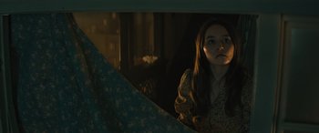 Movie still from “No One Will Save You” (2023), directed by Brian Duffield – A woman is standing in the dark looking out of a window; Medium shot, High angle