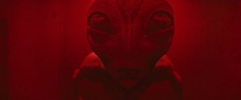 Movie still from “No One Will Save You” (2023), directed by Brian Duffield – An alien with a red background is looking at the camera; Extreme Close Up shot, Overhead angle