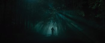 Movie still from “No One Will Save You” (2023), directed by Brian Duffield – A person standing in the middle of a dark forest at night; Extreme Wide shot, Low angle