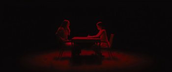 Movie still from “No One Will Save You” (2023), directed by Brian Duffield – Two people sitting at a table in a dark room; Wide shot, High angle
