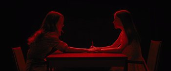 Movie still from “No One Will Save You” (2023), directed by Brian Duffield – Two women sitting at a table with a pen in their hand; Medium shot, Overhead angle