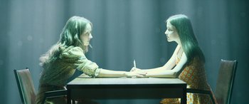 Movie still from “No One Will Save You” (2023), directed by Brian Duffield – Two young women sitting in front of each other at a table; Medium shot, High angle