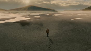 Movie still from “Noah” (2014), directed by Darren Aronofsky – A person is walking on the beach near the water; Extreme Wide shot, High angle