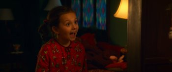 Movie still from “Noelle” (2019), directed by Marc Lawrence – A little girl in a red christmas pajamas is smiling; Medium shot, Over the shoulder angle