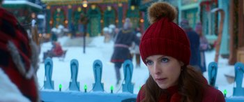 Movie still from “Noelle” (2019), directed by Marc Lawrence – A woman wearing a red hat sitting in front of blue chairs in the snow; Close Up shot, Over the shoulder angle