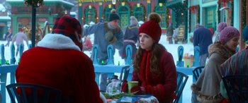 Movie still from “Noelle” (2019), directed by Marc Lawrence – A woman sitting at an outdoor table with a cup of coffee; Medium shot, Over the shoulder angle