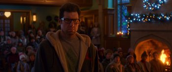 Movie still from “Noelle” (2019), directed by Marc Lawrence – A man with glasses is standing in front of a group of people; Close Up shot, Over the shoulder angle