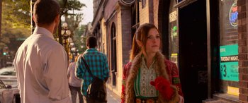 Movie still from “Noelle” (2019), directed by Marc Lawrence – A young woman in a colorful outfit standing on the sidewalk; Medium shot, Low angle