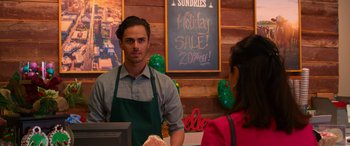 Movie still from “Noelle” (2019), directed by Marc Lawrence – A man standing in front of a woman behind a counter; Medium shot, Over the shoulder angle