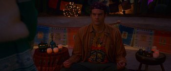 Movie still from “Noelle” (2019), directed by Marc Lawrence – A man sitting on the ground in a room with candles; Medium shot, High angle