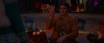 Movie still from “Noelle” (2019), directed by Marc Lawrence – A man sitting in front of a table holding up a peace sign; Medium shot, High angle