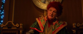 Movie still from “Noelle” (2019), directed by Marc Lawrence – An older man wearing a red wig and a colorful outfit; Close Up shot, Over the shoulder angle