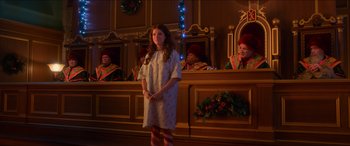 Movie still from “Noelle” (2019), directed by Marc Lawrence – A woman standing in front of a group of people in a room; Wide shot, Over the shoulder angle