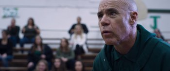 Movie still from “Notorious Nick” (2021), directed by Aaron Leong – An older man in a green shirt is in front of a group of people; Close Up shot, Over the shoulder angle