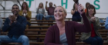 Movie still from “Notorious Nick” (2021), directed by Aaron Leong – A group of people sitting in a gym watching a game; Medium shot, Low angle