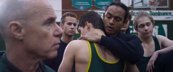 Movie still from “Notorious Nick” (2021), directed by Aaron Leong – A man hugging another man while others look on; Medium shot, Over the shoulder angle