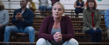 Movie still from “Notorious Nick” (2021), directed by Aaron Leong – A woman sitting on the ground in front of some people; Medium shot, Over the shoulder angle